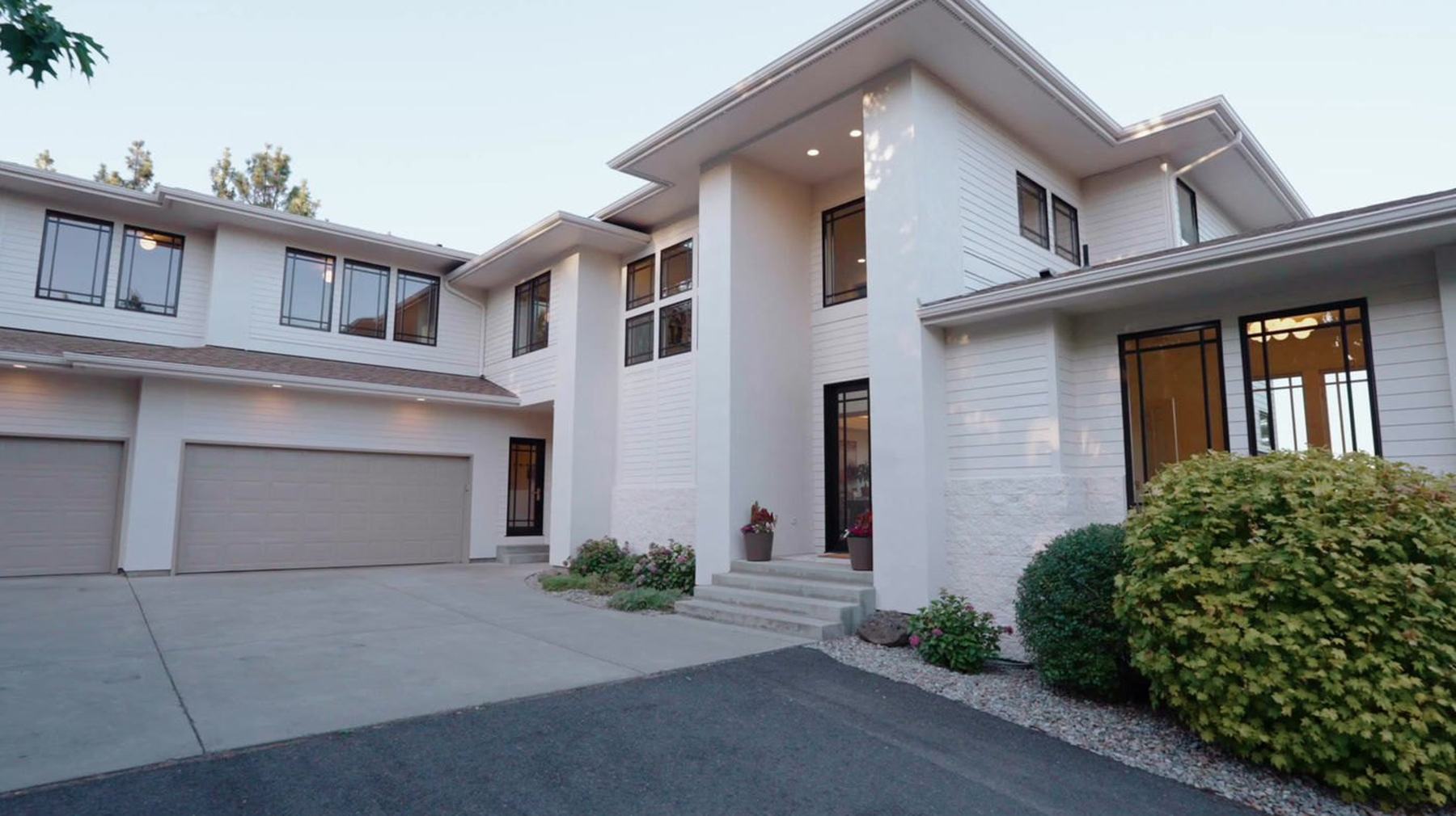 A modern white two-storey home photographed at dusk, warm light in the windows.